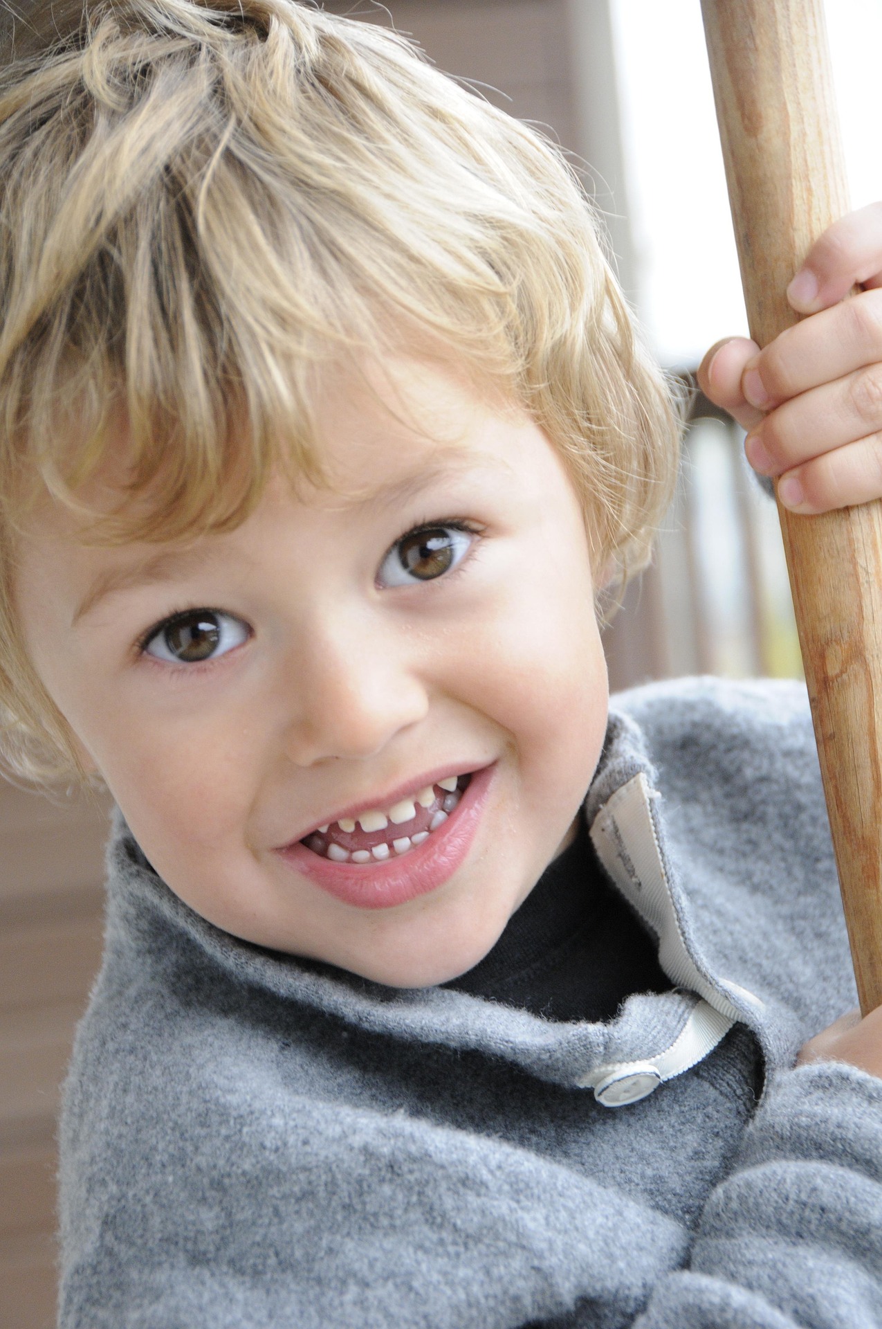kleiner Junge hält sich an einem Stock fest und lächelt mit braunen Augen und blonden Haaren in die Kamera