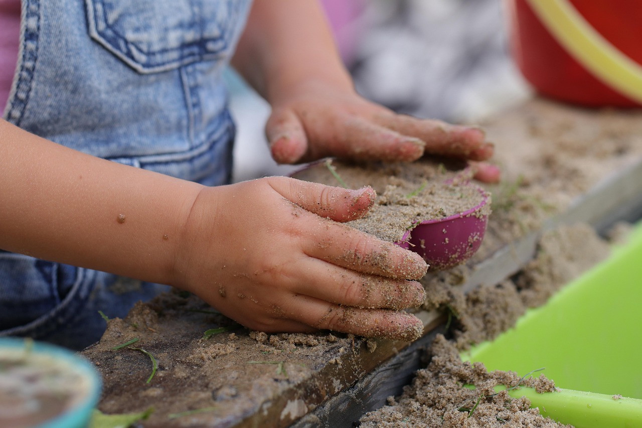 Ein kleines Kind hat mit seinen Händen ein Förmchen mit Sand befüllt. Die kleinen Hände umfassen es achtsam.